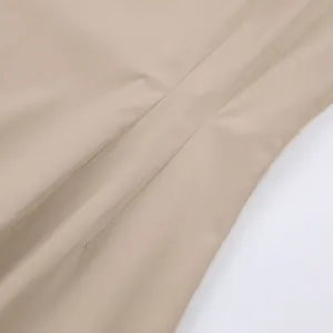Detailopname van het fijne stiksel en de gladde beige stoftextuur van de overhemdjurk
