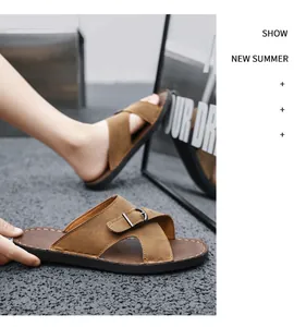 Close-up of brown cross-strap men's sandals featuring buckle detail on grey textured floor