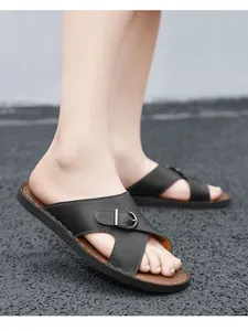 Detail view of men's black leather slide sandals with buckle on asphalt background.