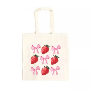 Detailed view of watercolor strawberry and pink bow prints on a canvas tote bag.