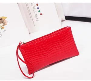 Detailopname van een felrode clutch met krokodillentextuur en polsbandje.
