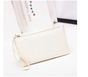 Gedetailleerde close-up van witte clutch met krokodillenpatroon en gouden ritsluiting