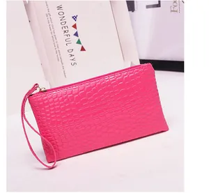 Gedetailleerde weergave van de felroze clutch met krokodillenprint en polsbandje.