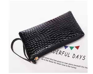 Detailweergave van een zwarte clutch met krokodillenpatroon, polsbandje en rits.