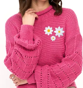 Close-up detail of white daisy embroidery patches applied on a pink knitted sweater