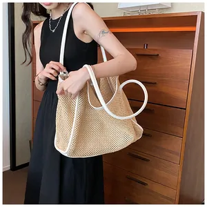 Große gewebte Strohtasche mit weißen Lederriemen, getragen von einem Modell für Sommer.