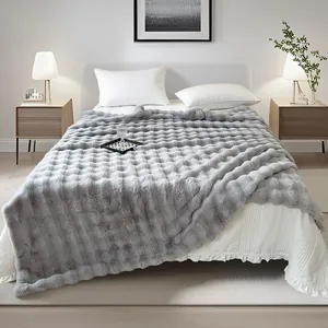 Couverture douce en fausse fourrure grise à texture bulles dans une chambre confortable.