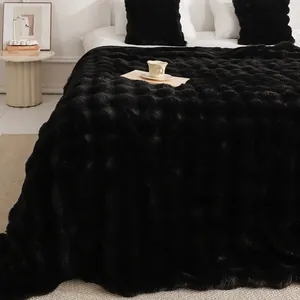 Couverture de luxe en fausse fourrure de lapin noire avec texture à bulles douce sur un lit.