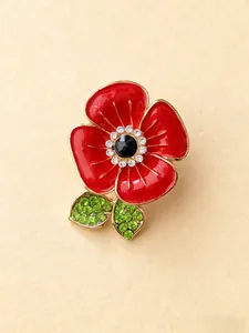 Gros plan d'une broche coquelicot en émail rouge avec cristaux verts et blancs étincelants