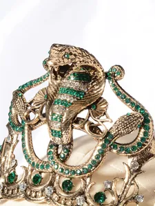 Detailopname van een barokke gouden cobrakroon met groene strass-details en kristallen.
