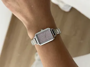Detailed macro view of a silver square quartz watch with a shimmering purple dial on a wrist.