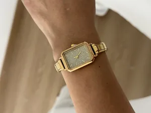Detailed view of an elegant gold rectangular watch with a glitter dial on a wrist