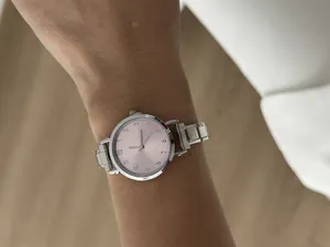 Close-up van een minimalistisch dameshorloge met roze wijzerplaat en zilveren band.