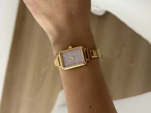 Elegant ladies' gold-tone square quartz watch with a glittery purple dial shown on a wrist