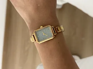 Close-up of elegant gold rectangular ladies quartz watch with glittery silver dial on wrist