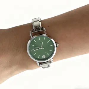 Close-up of a silver modular stainless steel watch with a green dial on a wrist.