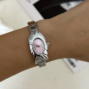 Close-up of a unique silver fish-shaped watch with a pink dial on a wrist