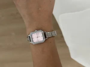 Gros plan d'une montre à quartz carrée avec lunette en cristal et cadran rose élégant