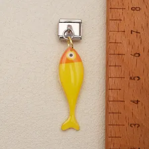Gros plan sur breloque poisson jaune sur lien modulaire italien avec règle bois