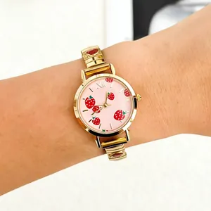 Close-up of a stylish gold strawberry wristwatch with a pink dial worn on a female wrist.