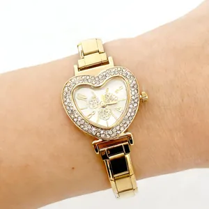 Detail shot of a luxury gold heart-shaped watch with rhinestone bezel on a wrist.