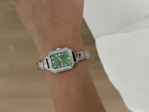 Détail d'une montre carrée argentée pour femme avec cadran vert et cristaux brillants.