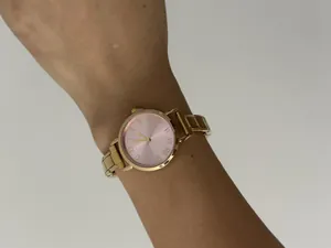 Elegant dameskwartshorloge met roze wijzerplaat met Romeinse cijfers en gouden armband.