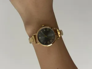 Elegante gouden dameshorloge met zwarte Romeinse cijfers en modulaire band om pols.