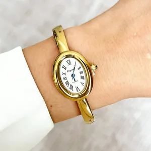Gedetailleerde close-up van een elegant gouden ovaal horloge met Romeinse cijfers om een pols