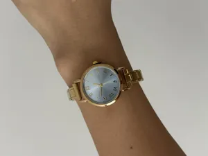 Detailopname van een goudkleurig dameshorloge met afneembare band, gedragen om de pols.
