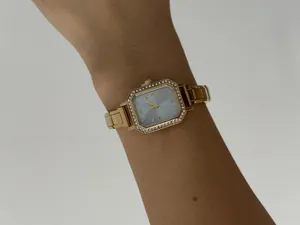 Gros plan d'une montre à quartz dorée carrée pour femme avec lunette en strass.