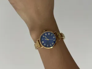 Detailopname van een goudkleurig dameshorloge met blauwe wijzerplaat om de pols gedragen