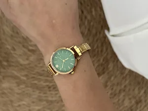 Close-up of a gold modular watch with a vibrant green glitter dial worn on a wrist.