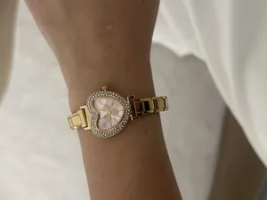 Close-up view of elegant heart-shaped gold watch with pink dial and rhinestones on wrist