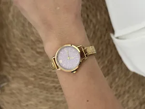 Detail view of a gold-tone modular link watch with a shimmering pink face on a wrist.