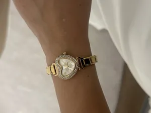 Close-up of elegant gold heart-shaped watch with rhinestones on a lady's wrist.