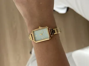 Detailed view of an elegant gold rectangular quartz watch with a mint green dial on a wrist