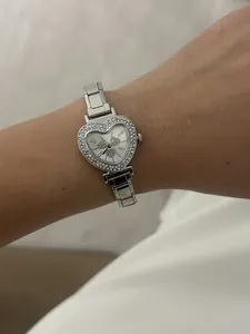 Close-up of a women's silver-tone heart-shaped watch with rhinestone bezel and link strap