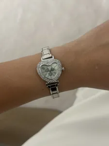 Detailed view of women's heart-shaped silver watch with rhinestone bezel and steel strap