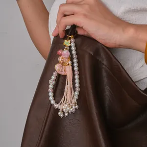Detailed macro view of an elegant pink gourd tassel charm with pearls on a brown leather bag