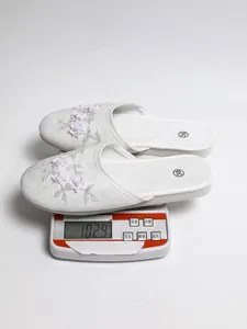 Vista ravvicinata di pantofole bianche floreali su una bilancia digitale da 102,9g