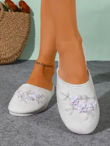 Primo piano di pantofole bianche in camoscio con fiori di paillettes e consistenza