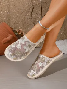 Detailansicht eleganter Mesh-Mules mit Blumenstickerei an den Füßen des Models.