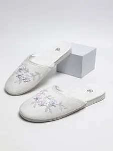 Vista dettagliata di pantofole bianche di peluche con eleganti decorazioni floreali di paillettes.