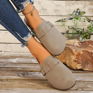 Vue détaillée de sabots taupe en suédine avec boucle réglable sur fond rustique