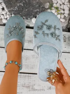 Dettaglio di ciabatte in velluto blu con ricamo floreale argento e paillettes.