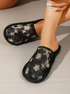 Detaillierte Nahaufnahme der floralen Stickerei auf schwarzen flachen Mesh-Mule-Hausschuhen
