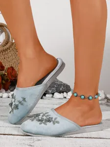 Dettaglio di pantofole in velluto azzurro con raffinati ricami floreali e perline applicate.