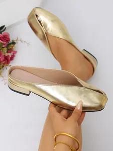 Detalle de elegantes chinelas planas doradas metalizadas con un diseño único de abertura