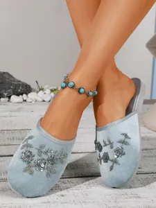 Dettaglio di pantofole in velluto azzurro con ricami floreali su pedana di legno